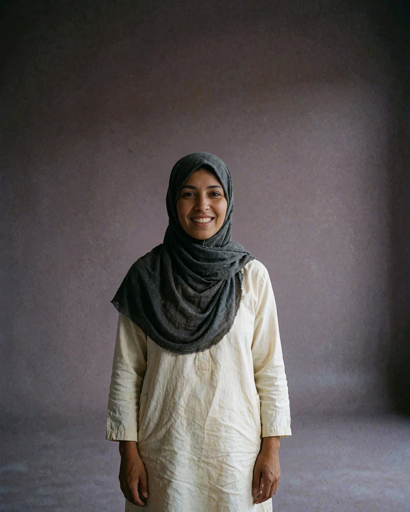 Yemeni member in a charcoal headscarf and cream tunic smiling warmly in a plain studio setting