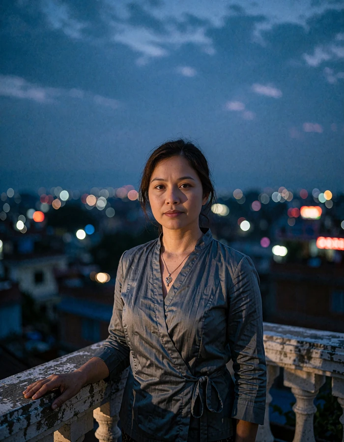 Nepali member in a slate grey wrap blouse standing on a rooftop terrace at blue hour